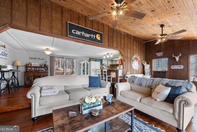 living area with ceiling fan, wood walls, wood finished floors, wooden ceiling, and a wealth of natural light