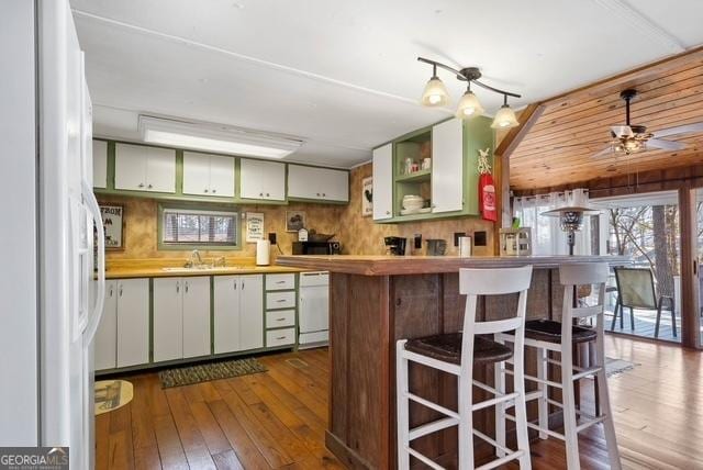 kitchen with a breakfast bar area, a ceiling fan, a sink, dark wood-style floors, and white appliances