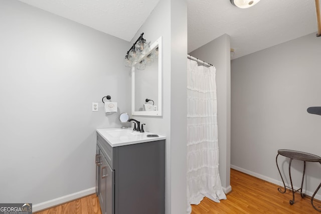 bathroom with a textured ceiling, baseboards, vanity, and wood finished floors