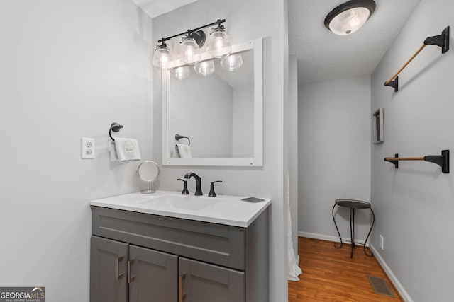 bathroom featuring visible vents, a textured ceiling, vanity, wood finished floors, and baseboards