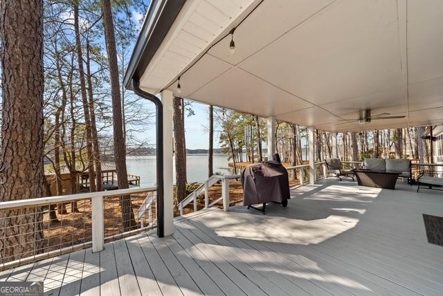 wooden terrace featuring an outdoor hangout area, area for grilling, a ceiling fan, and a water view