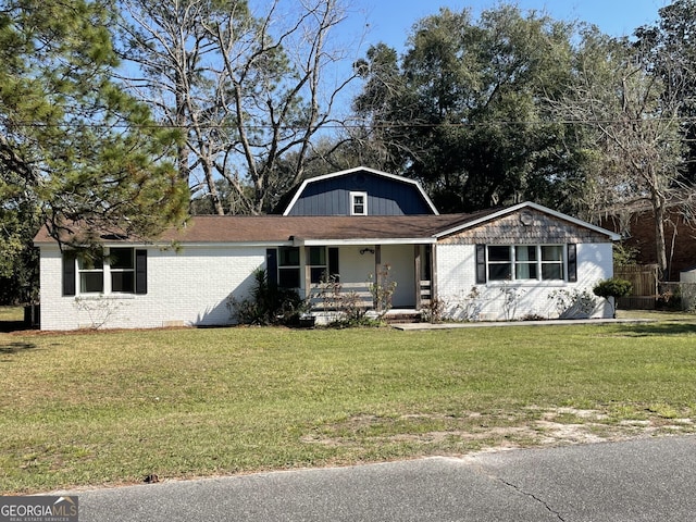 view of front of home with a gambrel roof, covered porch, brick siding, and a front lawn