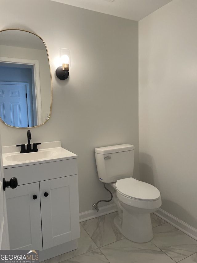 half bathroom featuring marble finish floor, vanity, toilet, and baseboards