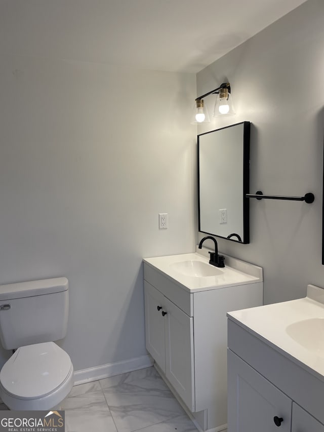 bathroom featuring marble finish floor, two vanities, toilet, a sink, and baseboards