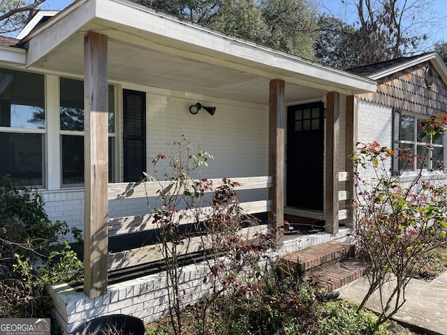 view of exterior entry featuring covered porch and brick siding