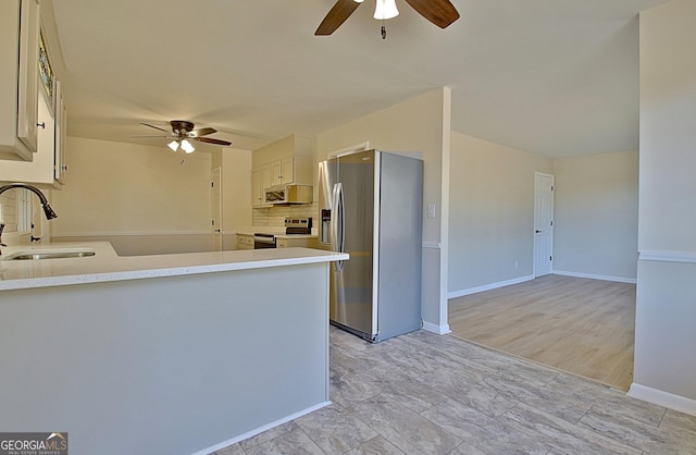 kitchen with light countertops, backsplash, appliances with stainless steel finishes, a sink, and a peninsula