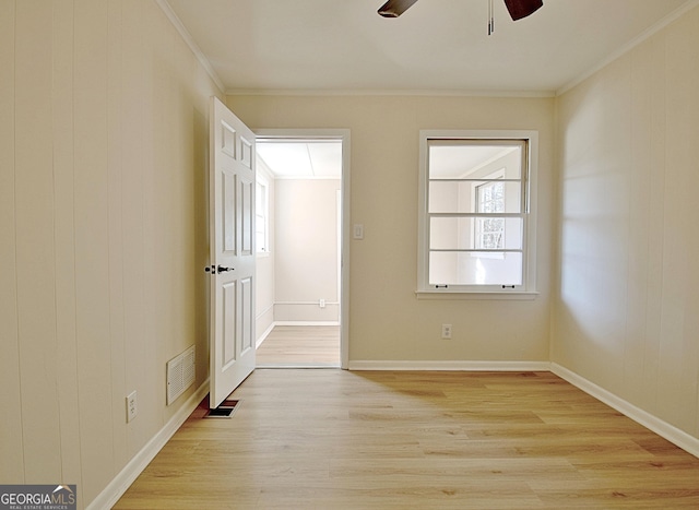 empty room with light wood-style flooring, visible vents, and crown molding