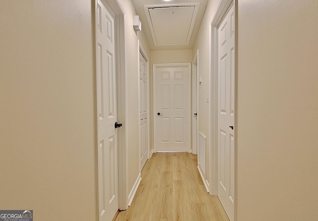 corridor featuring light wood finished floors, attic access, and baseboards