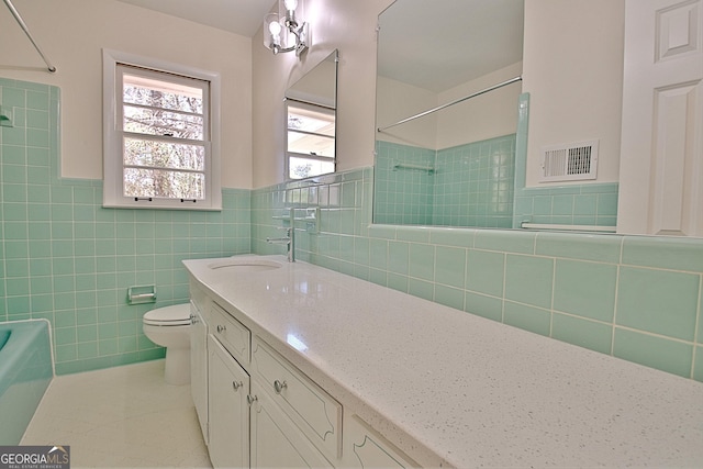 bathroom with visible vents, toilet, tile patterned flooring, vanity, and tile walls