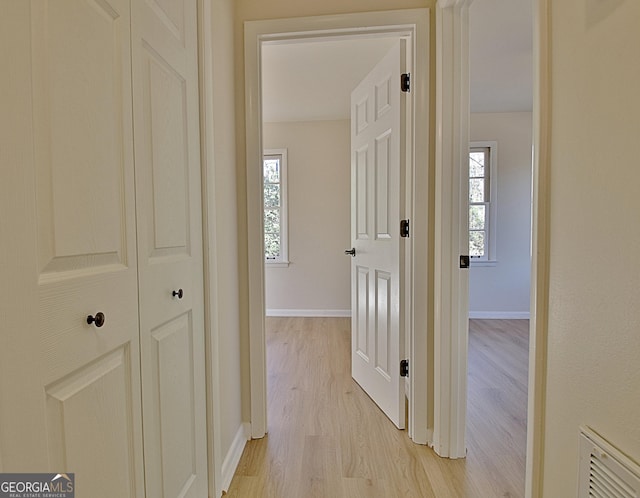 hallway with visible vents, light wood-style flooring, and baseboards