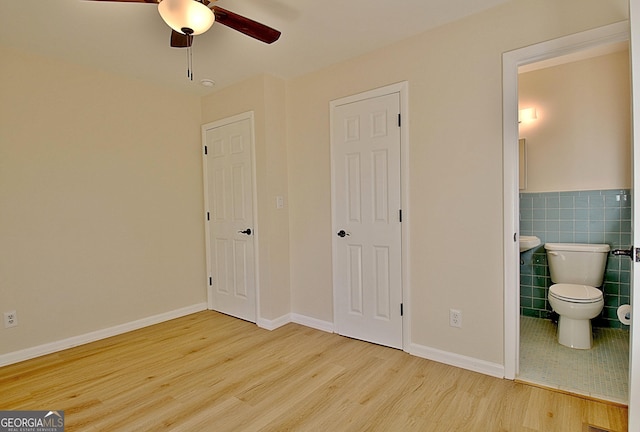 bedroom featuring baseboards, tile walls, ensuite bathroom, and wood finished floors