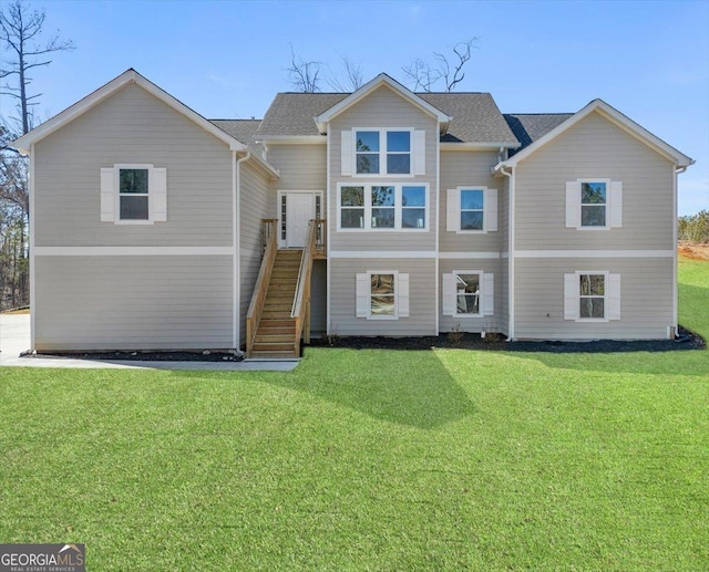 view of front facade featuring stairs, roof with shingles, and a front yard