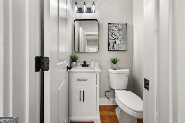 bathroom featuring toilet, baseboards, wood finished floors, and vanity