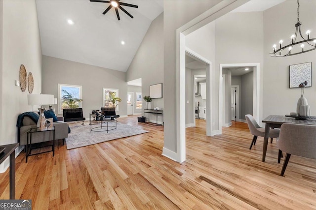 living area featuring baseboards, high vaulted ceiling, light wood-type flooring, and a notable chandelier