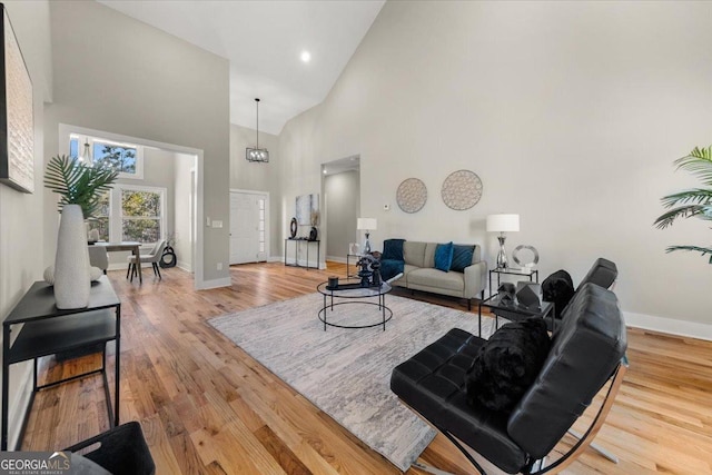 living area with high vaulted ceiling, light wood finished floors, and baseboards