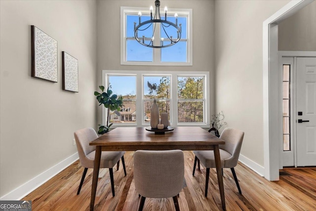 dining room featuring a towering ceiling, baseboards, a notable chandelier, and wood finished floors