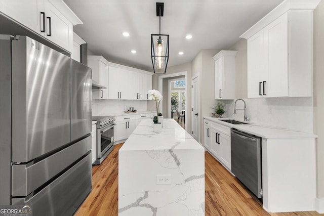 kitchen with appliances with stainless steel finishes, white cabinets, a sink, and a center island