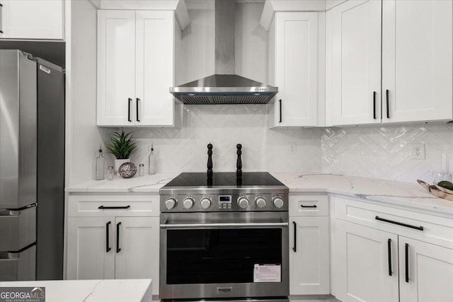 kitchen featuring appliances with stainless steel finishes, white cabinetry, wall chimney range hood, and light stone counters