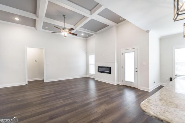 unfurnished living room featuring baseboards, coffered ceiling, a glass covered fireplace, a towering ceiling, and dark wood-type flooring