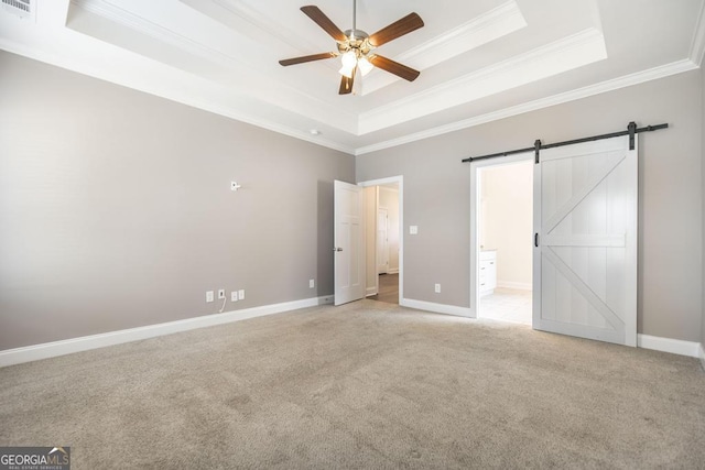 unfurnished bedroom featuring a barn door, a raised ceiling, crown molding, and light colored carpet