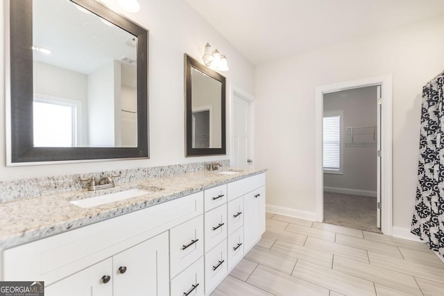 full bath with double vanity, a spacious closet, a sink, and baseboards