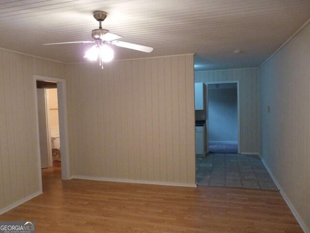 empty room featuring ornamental molding, ceiling fan, baseboards, and wood finished floors