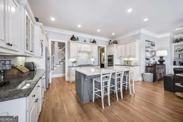 kitchen featuring light wood finished floors, white cabinets, ornamental molding, a kitchen breakfast bar, and a kitchen island with sink