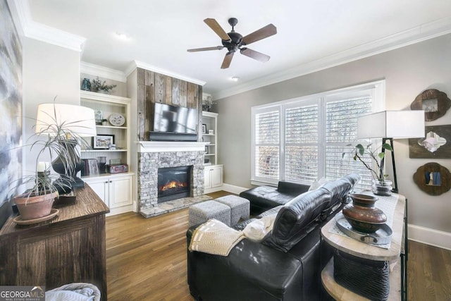 living room with baseboards, ceiling fan, ornamental molding, wood finished floors, and a stone fireplace