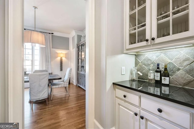 bar featuring tasteful backsplash, dark wood-type flooring, crown molding, and baseboards