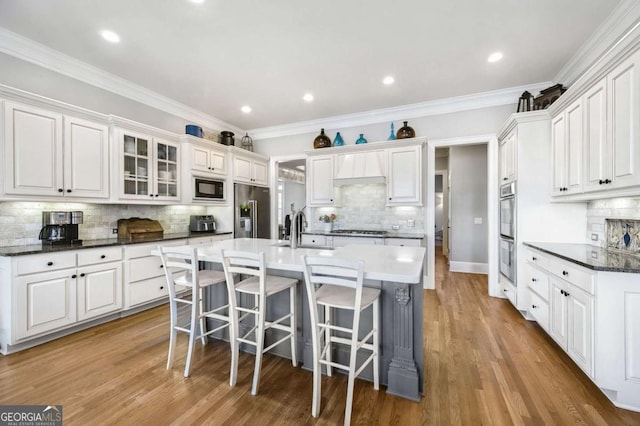 kitchen featuring a center island with sink, a breakfast bar, wood finished floors, stainless steel appliances, and a sink