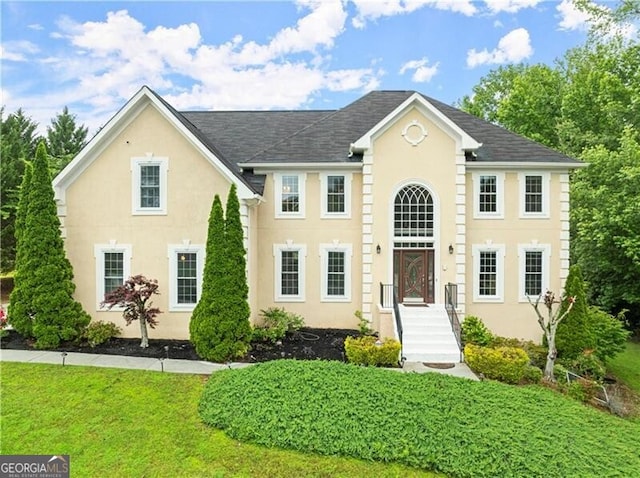 colonial home featuring a front lawn and stucco siding