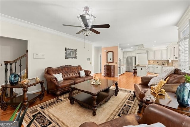 living area featuring light wood-style floors, stairway, ornamental molding, and a ceiling fan