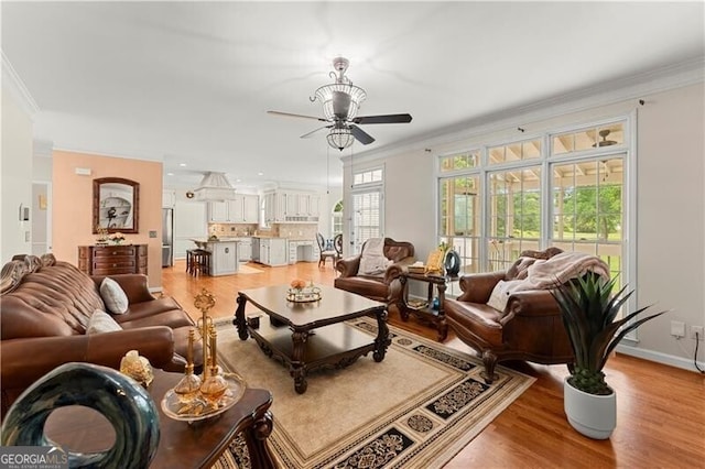 living area featuring ornamental molding, baseboards, ceiling fan, and light wood finished floors