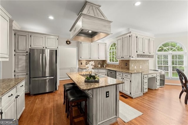 kitchen with tasteful backsplash, light stone countertops, custom exhaust hood, stainless steel appliances, and crown molding