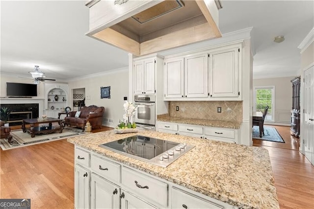 kitchen featuring black electric stovetop, a premium fireplace, stainless steel oven, light wood finished floors, and crown molding