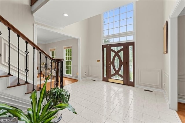 entrance foyer with light tile patterned floors, wainscoting, stairway, ornamental molding, and a decorative wall