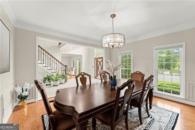 dining room with light wood-style floors, ornamental molding, a decorative wall, and a chandelier