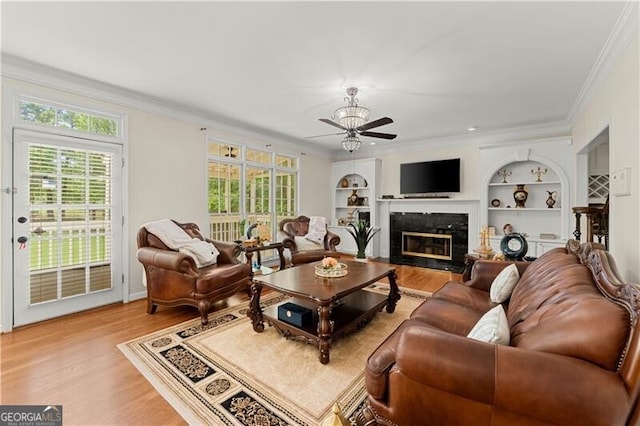 living area with crown molding, built in shelves, a high end fireplace, and light wood-style floors