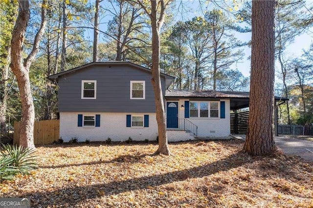 split level home with a carport, brick siding, crawl space, and fence