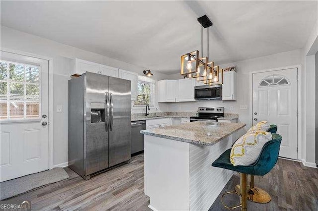 kitchen with light stone counters, a kitchen island, wood finished floors, white cabinetry, and appliances with stainless steel finishes