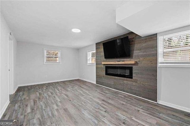 unfurnished living room featuring a glass covered fireplace, baseboards, and wood finished floors