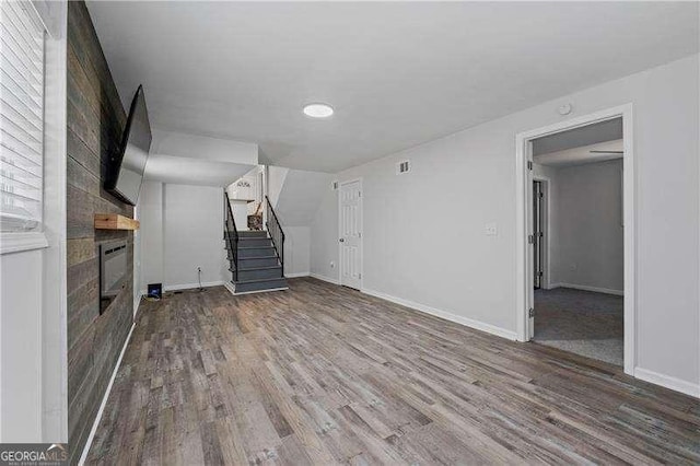 unfurnished living room featuring stairway, wood finished floors, and baseboards