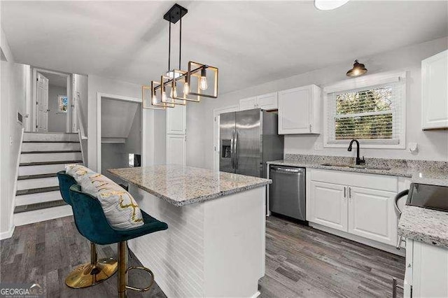 kitchen featuring appliances with stainless steel finishes, dark wood-type flooring, white cabinets, a sink, and a kitchen island