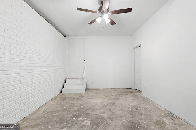 spare room featuring brick wall, ceiling fan, and unfinished concrete flooring