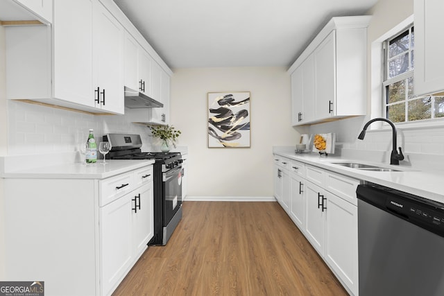 kitchen with under cabinet range hood, a sink, stainless steel dishwasher, light wood finished floors, and gas range oven