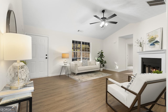 living area featuring lofted ceiling, a warm lit fireplace, visible vents, and wood finished floors