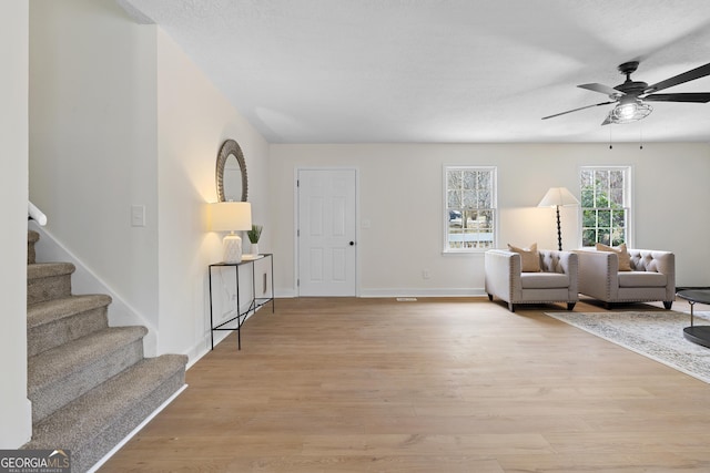 living area featuring light wood-style floors, stairway, baseboards, and a ceiling fan