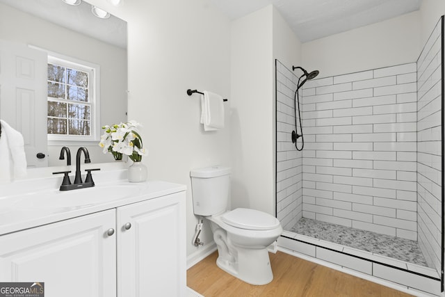 full bathroom featuring toilet, a tile shower, vanity, wood finished floors, and baseboards