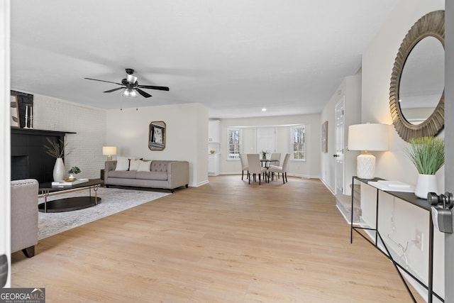 living area with light wood-type flooring, baseboards, ceiling fan, and brick wall