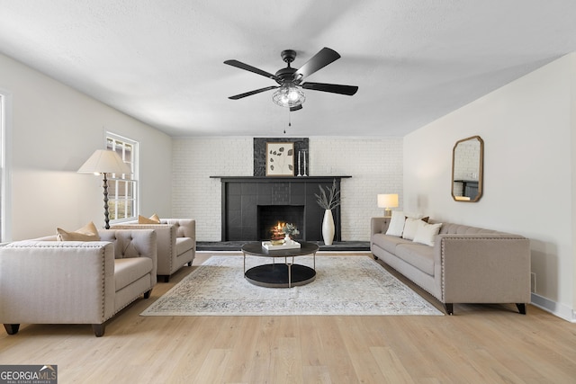 living area featuring a brick fireplace, a textured ceiling, a ceiling fan, and wood finished floors